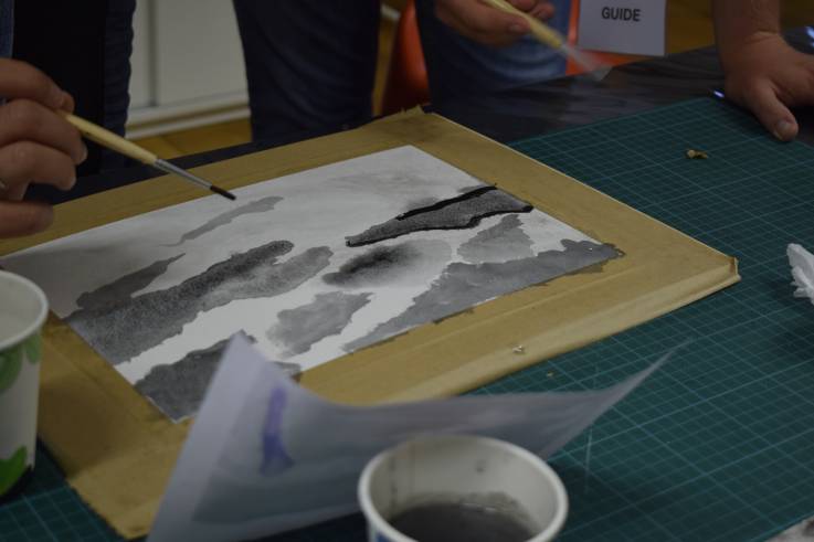 Die Hand einer Person malt mit schwarzer Aquarellfarbe auf ein Blatt Papier